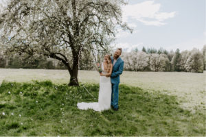 Bride and groom standing in a field with mountains popping open a bottle of champaigne